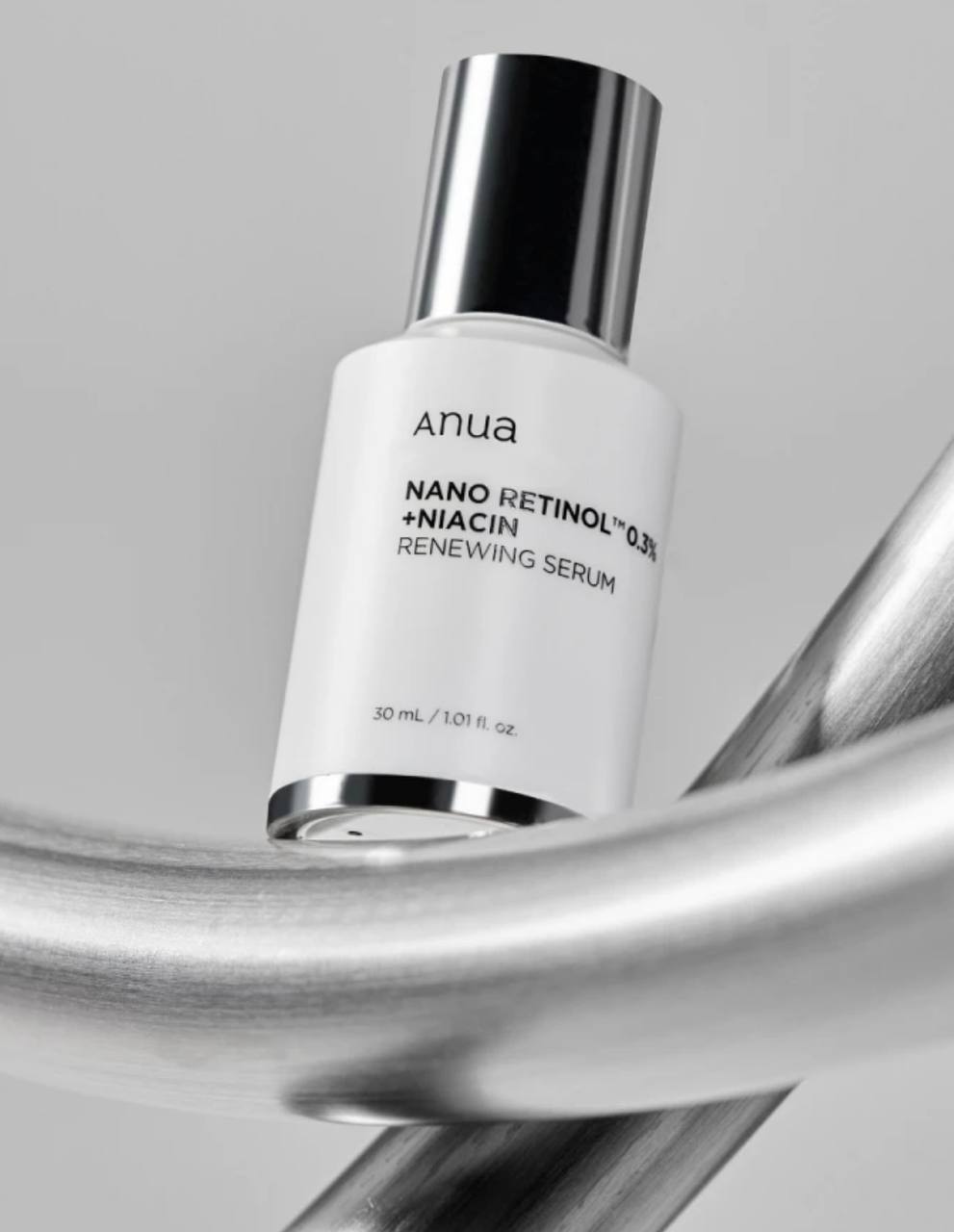 На металевій конструкції стоїть біла пляшечка з темно-сірою кришечкою засобу Anua Nano Retinol 0,3% + Niacin Renewing.