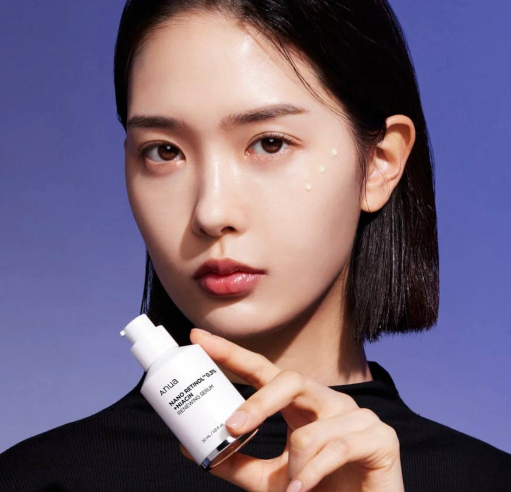 Дівчина азіатської зовнішності тримає пальцями відкриту пляшечку засобу Anua Nano Retinol 0,3% + Niacin Renewing, під оком видно краплі засобу.