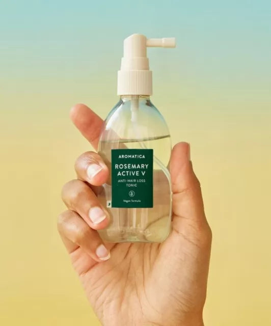 Прозора пляшечка з білим дозатором засобу Aromatica Rosemary Active V Anti-Hair Loss Tonic у руці на жовтому-блакитному фоні, 100 мл
