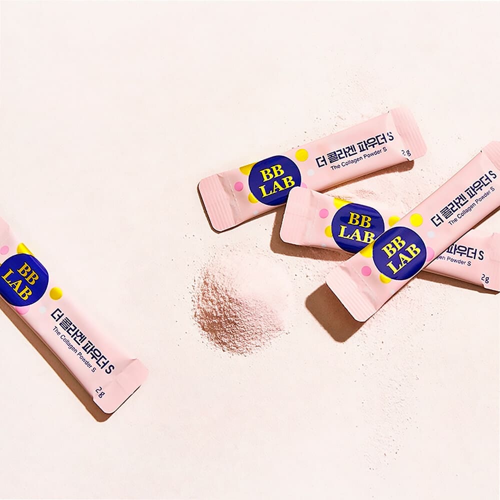 Чотири саше колагену BB Lab The Collagen Powder S Plus лежать на поверхні, поряд розсипаний порошок колагену.