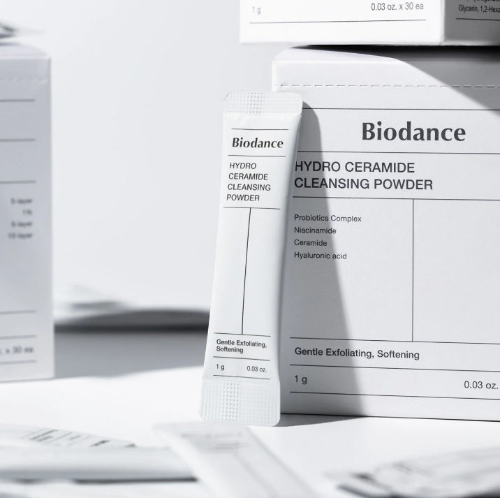 На білу коробку засобу BIODANCE Hydro Ceramide Cleansing Powder оперте саше, довкола видно інші білі коробки.