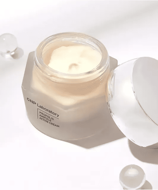 Відкрита баночка крему CNP Laboratory Propolis Cream стоїть на білому фоні, а кришечка оперта на саму баночку.