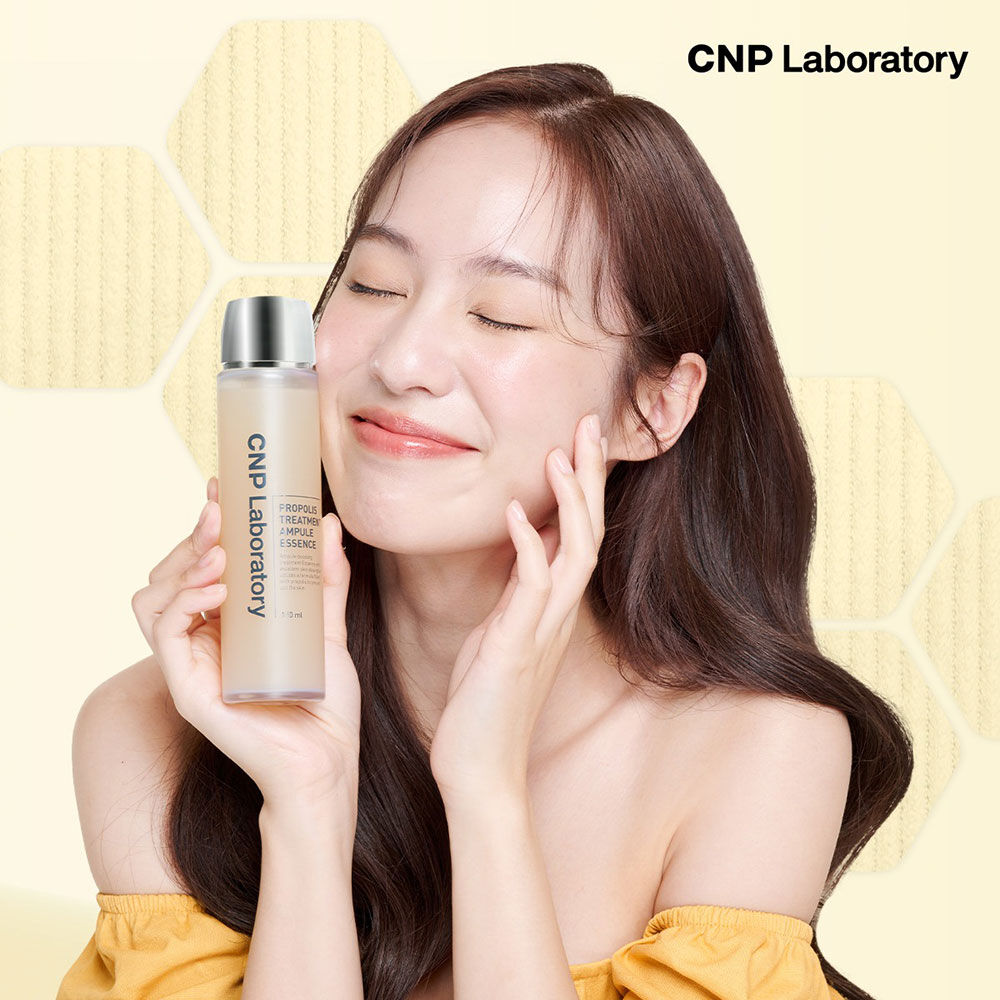 Дівчина з закритими очима та посмішкою тримає пляшечку CNP Laboratory Propolis Treatment Ampoule Essence біля обличчя.
