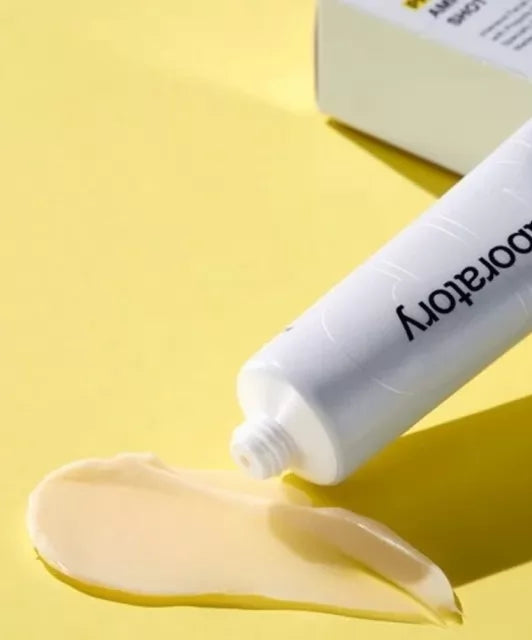 Відкритий тюбик CNP Laboratory Propolis Cream білий з чорними написами лежить на жовтій поверхні, поруч розмазаний крем з кремовою текстурою жовтуватого кольору.