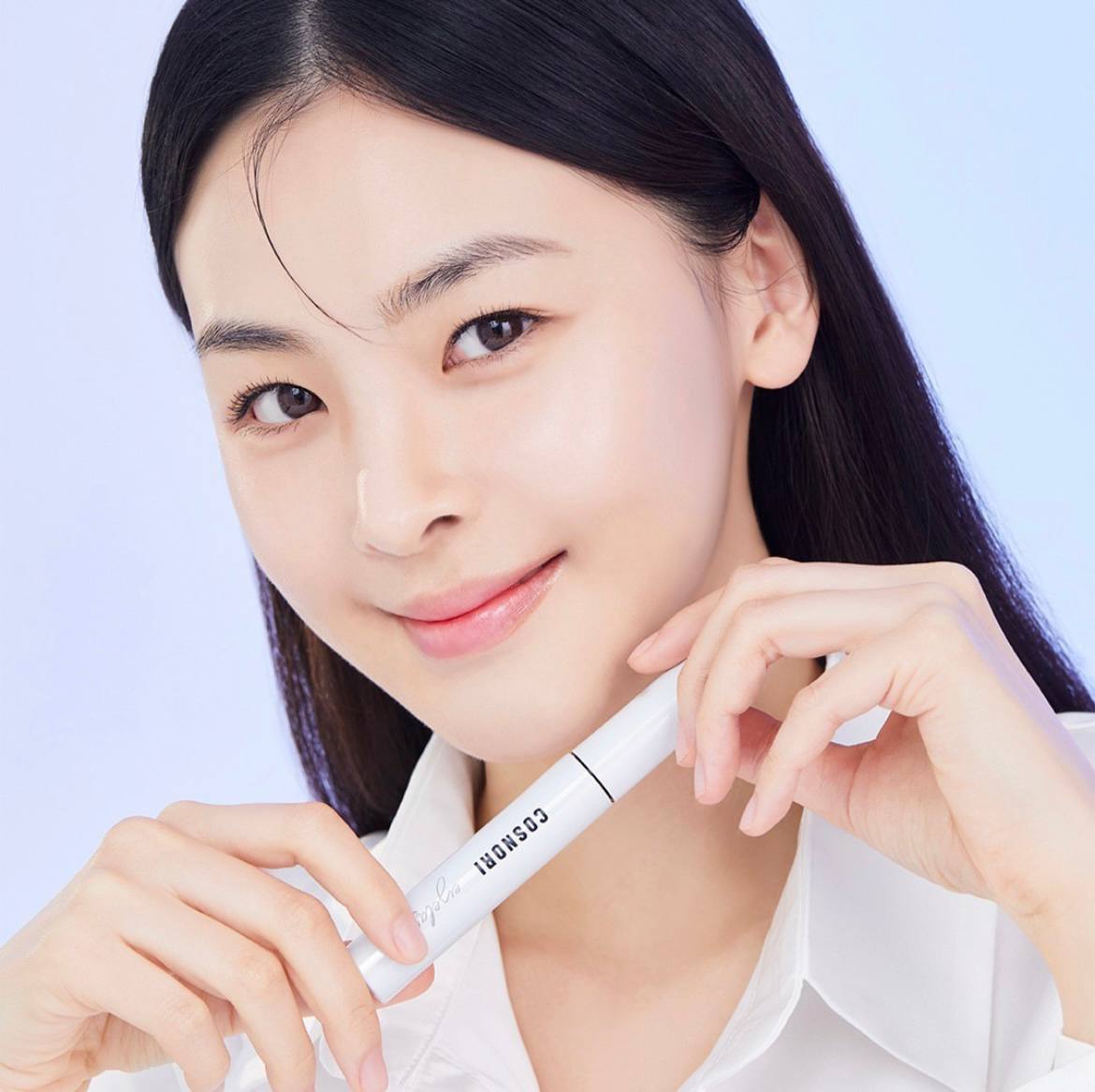 Дівчина азіатської зовнішності тримає флакон сироватки COSNORI Lash Serum в руках біля шиї та посміхається.