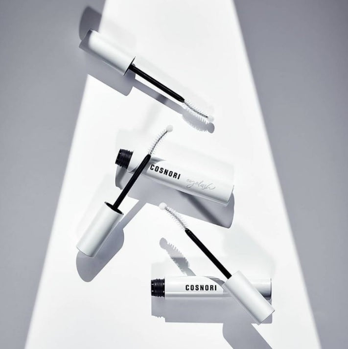 Декілька відкритих флаконів сироватки COSNORI Lash Serum та паличок для нанесення лежать на білій поверхні