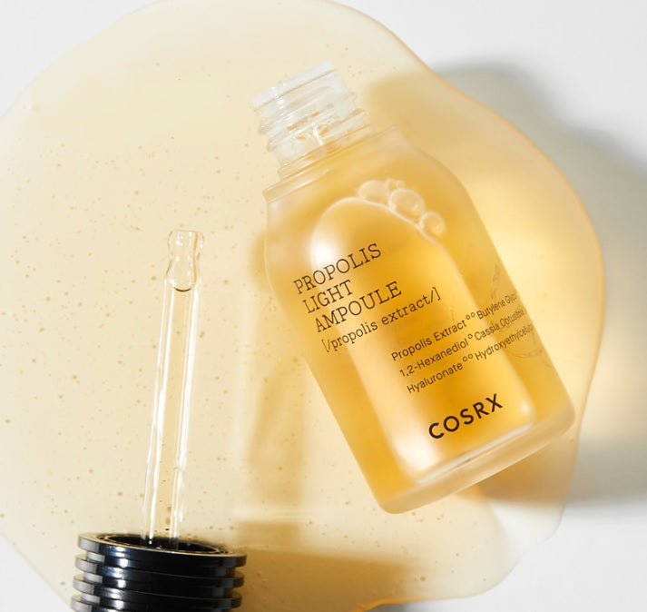Відкритий флакон COSRX Propolis Essence лежить поряд з піпеткою, з якої витікає есенція