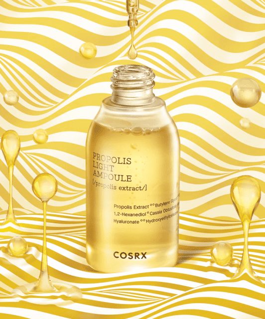 Відкритий флакон COSRX Propolis Essence стоїть на біло-жовтій полосатій поверхні, навколо літають краплі есенції.