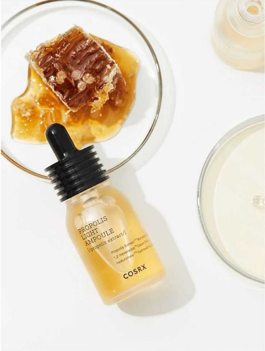 Закрита пляшечка COSRX Propolis Essence лежить на скляній тарілочці, на якій знаходиться шматочок медових сот.