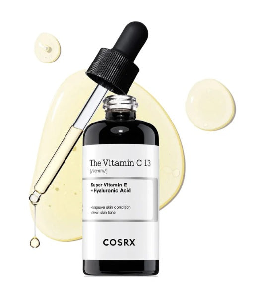 Відкрита пляшечка сироватки COSRX The Vitamin C 23 Serum стоїть, над нею піпетка, в яку набрана сироватка, і з неї капає засіб, показуючи текстуру. На фоні видно текстуру самого засобу.