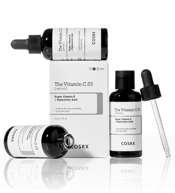 Упаковка, на якій лежить закрита пляшечка COSRX The Vitamin C 23 Serum, поруч стоїть відкрита пляшечка, а також біля неї лежить ще одна відкрита пляшечка цього засобу.