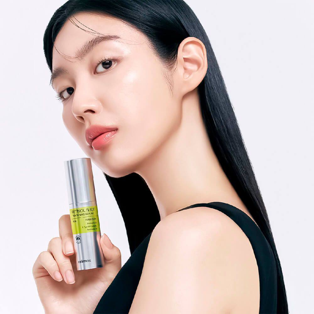 Дівчина азіатської зовнішності тримає пляшечку сироватки Celimax The Vita-A Retinol Shot Tightening Serum біля шиї.