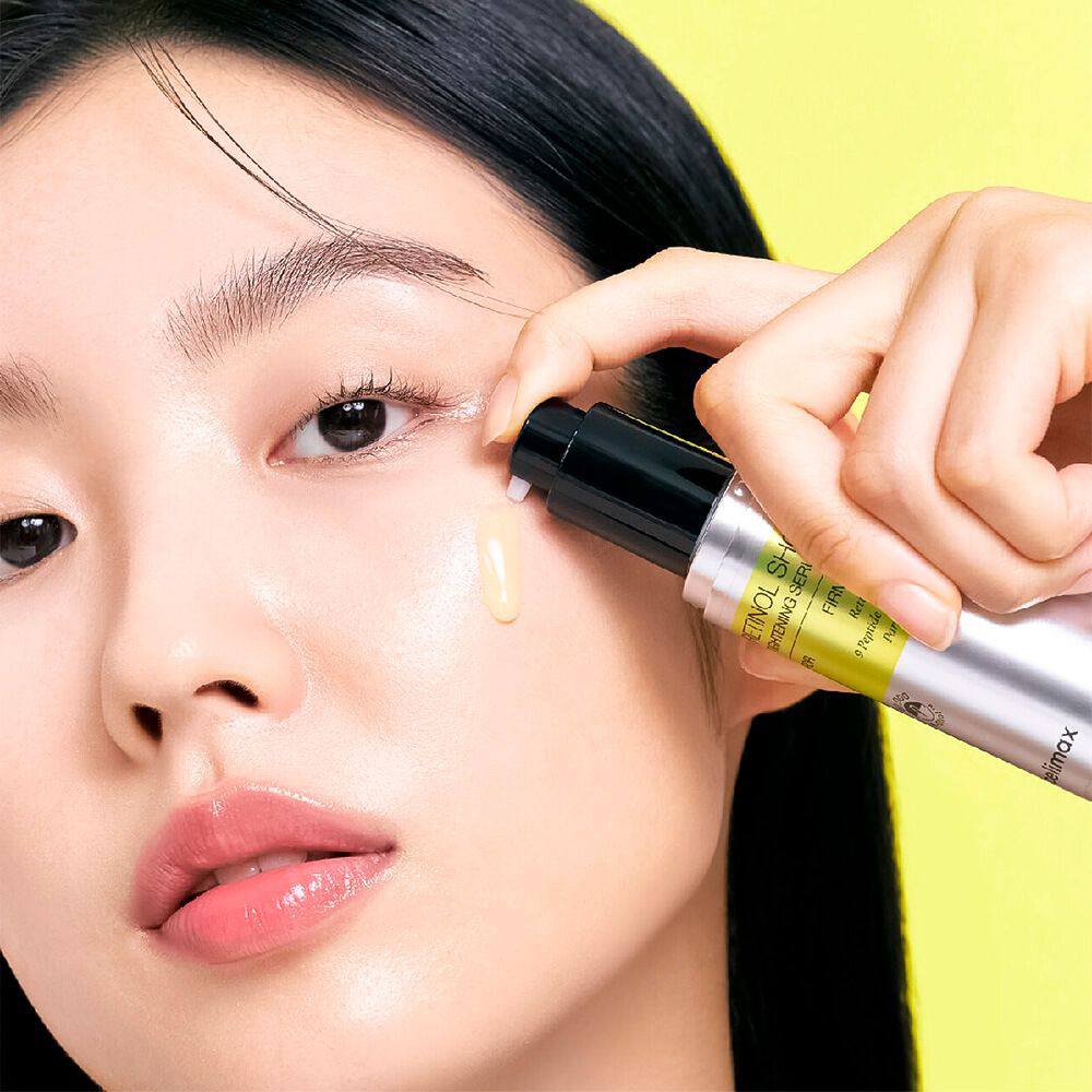 Дівчина азіатської зовнішності наносить сироватку Celimax The Vita-A Retinol Shot Tightening Serum під око.