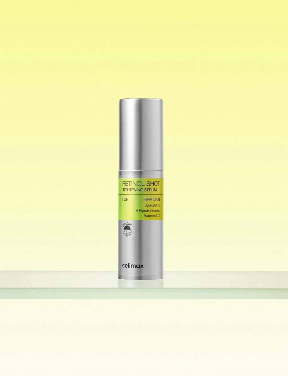 Срібляста пляшка сироватки Celimax The Vita-A Retinol Shot Tightening Serum стоїть на скляній поверхні на жовтому фоні.