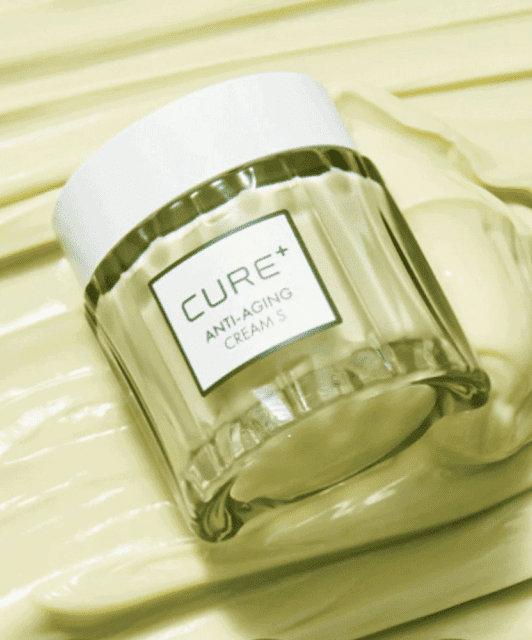 Баночка крему Cure Anti-Aging Cream лежить на зеленій кремовій поверхні.